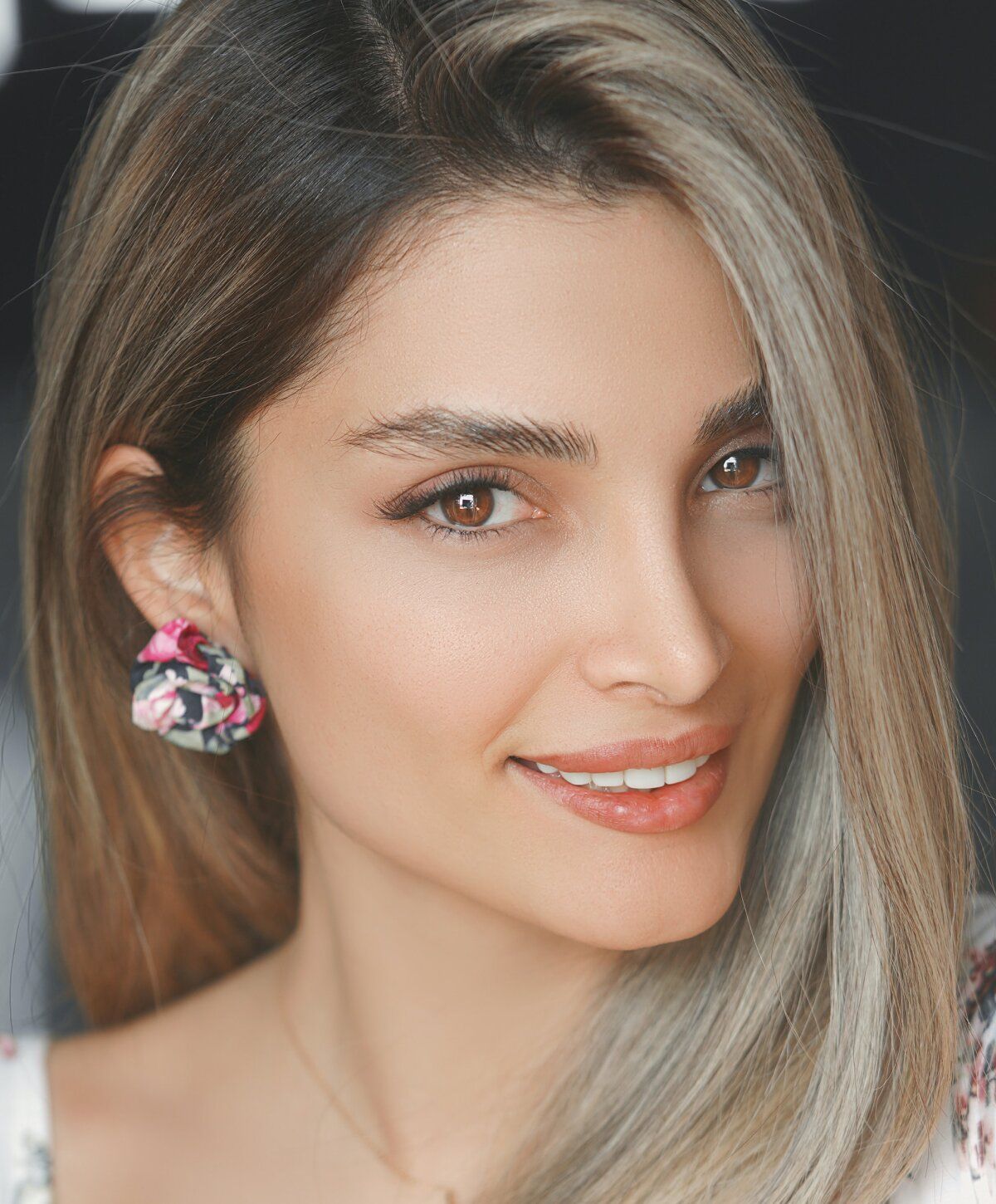 Smiling woman with wavy hair and floral earrings.