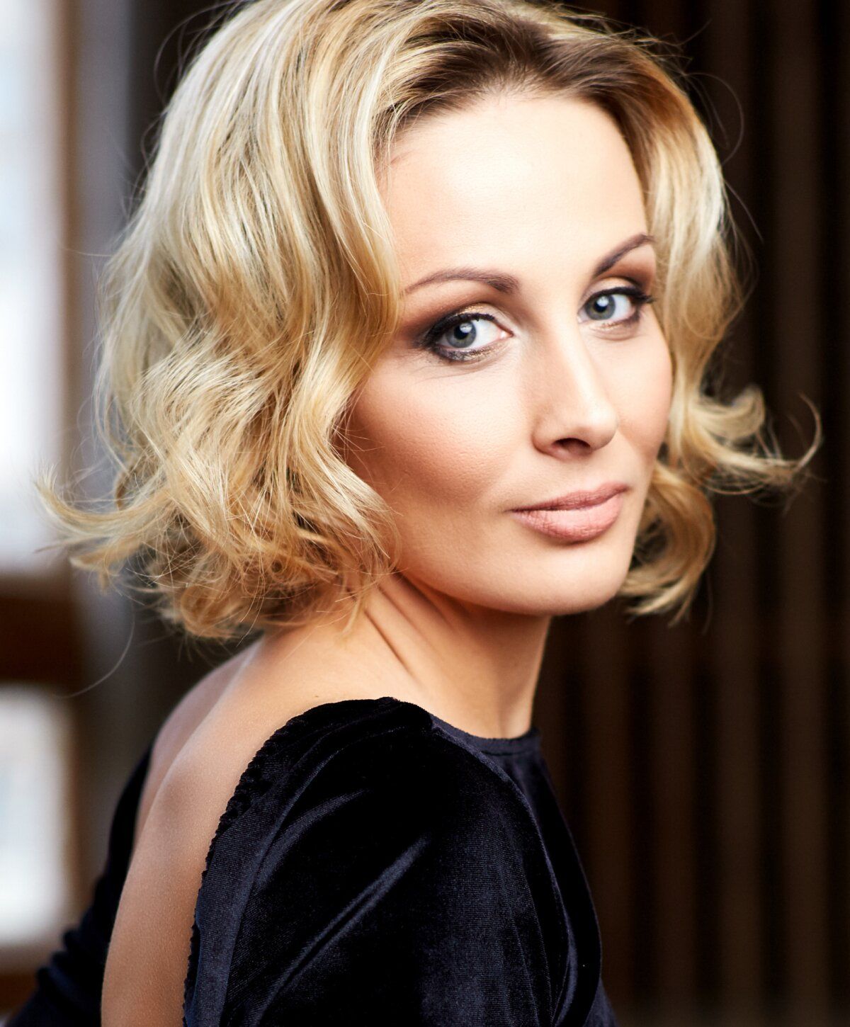 Woman with blonde wavy hair and elegant attire.