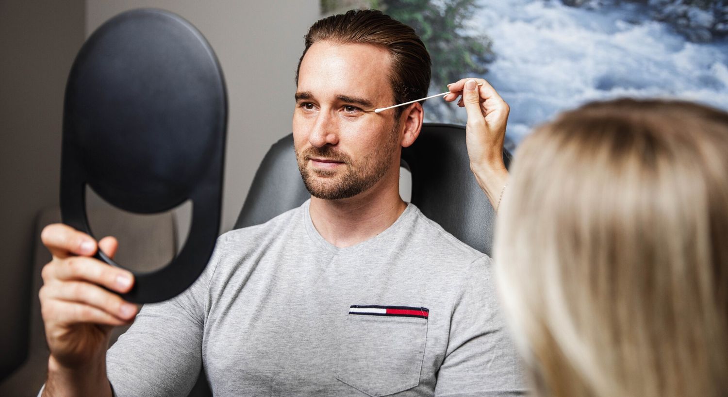 Man holding mirror during beauty treatment session.