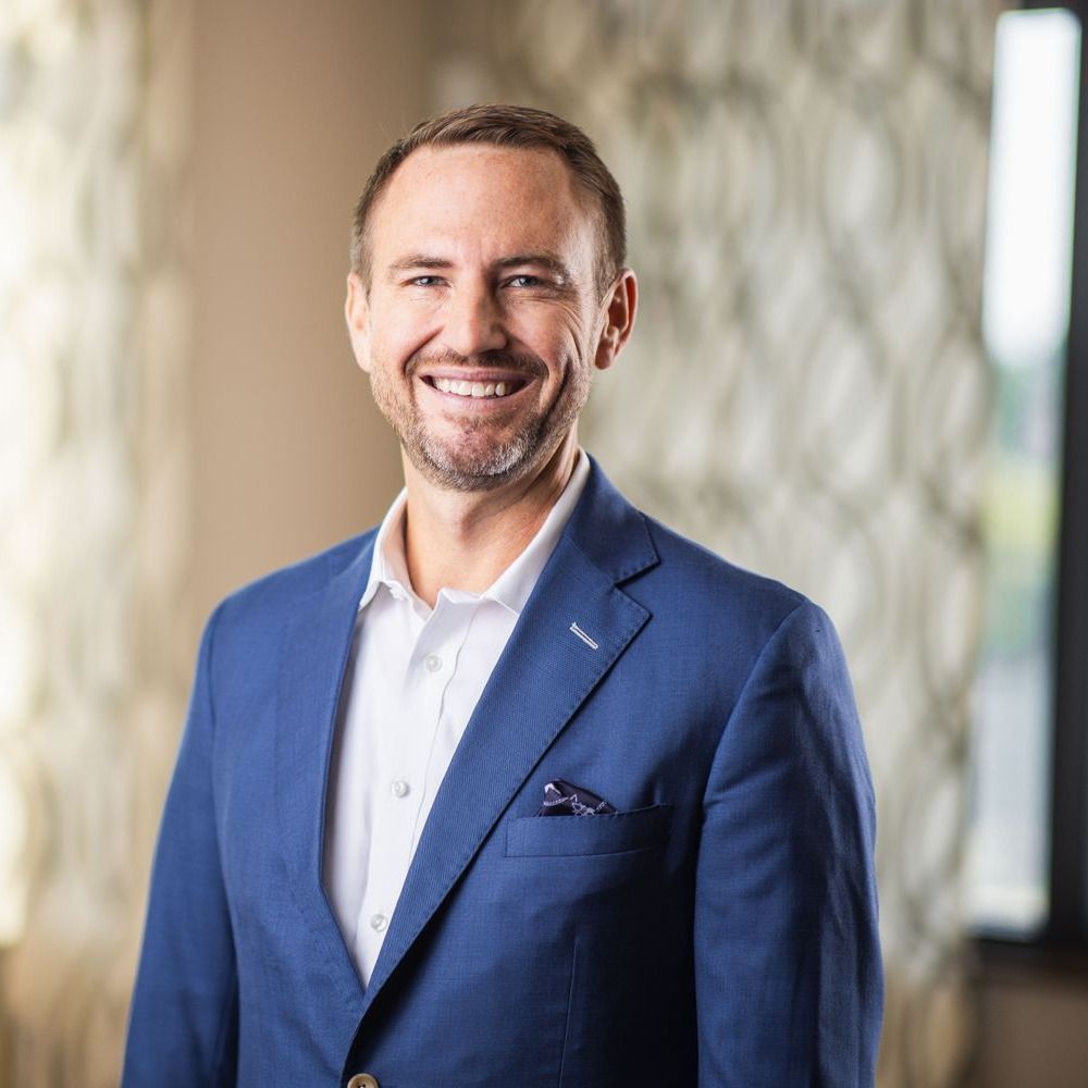 Smiling man in a blue suit backdrop.